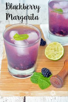 blackberry margarita with lime and mint garnish on a cutting board next to two glasses