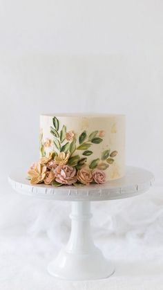 a white cake with flowers on it sitting on top of a table in front of a white backdrop