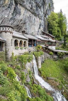 a waterfall running through a lush green forest next to a tall rock face covered in greenery