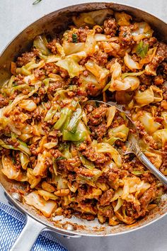 a large skillet filled with cabbage and ground beef, on top of a blue towel