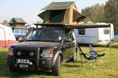 an suv with a camper attached to it parked in the grass next to other vehicles