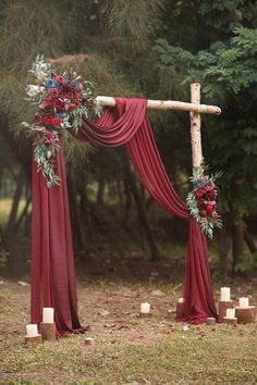 a wooden cross decorated with red flowers and greenery sits in the middle of an outdoor ceremony