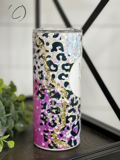 a pink and gold can sitting on top of a table next to a green plant