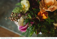 an arrangement of flowers and greenery in a vase on a counter top, with the focus on the center piece