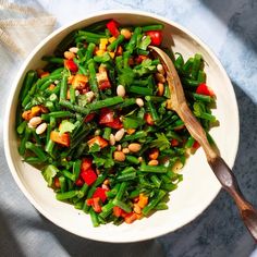 a white bowl filled with green beans and other veggies next to a wooden spoon