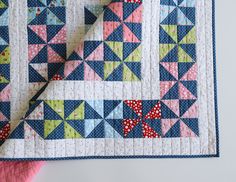 a blue and pink quilt on top of a white table with a piece of cloth next to it