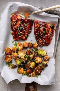 two pieces of meat and some vegetables on a sheet of paper with chopsticks