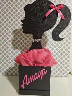 a black box with a pink bow on it that says amaya in front of a silhouette of a woman's head