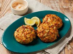 two chicken patties on a blue plate with lemon wedges and a cup of coffee