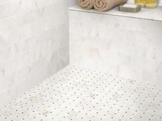 towels and soaps are on the ledge of a white tiled bathtub, along with two bottles of orange juice