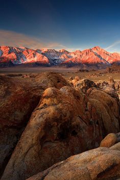 the mountains are covered in snow and rock formations at sunset, with bright sunlight on them