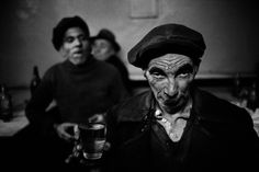 black and white photograph of two men with face paint on their faces, one holding a cup