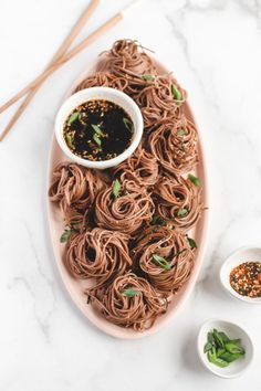 a plate full of noodles and dipping sauces on a marble counter top with chopsticks