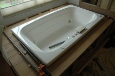 a large white bath tub sitting on top of a wooden counter next to a window