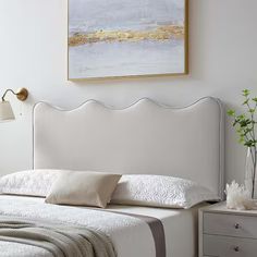 a white bed sitting under a painting next to a night stand