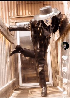 a woman in black leather clothes and hat standing on steps with her legs spread out