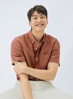 a man sitting on top of a white stool smiling at the camera with his arms crossed