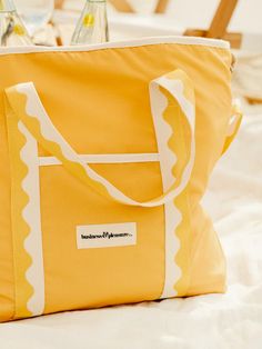 a yellow and white tote bag sitting on top of a bed next to bottles