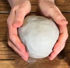 two hands holding a ball of dough on top of a wooden table