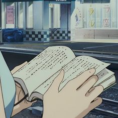 an anime character is reading a book on the train tracks in front of a building