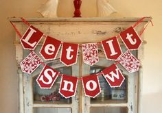 a red and white banner that says let it snow in front of an old window