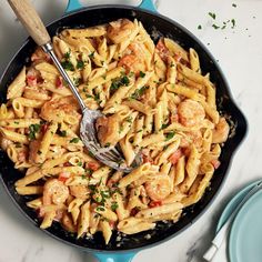 a skillet filled with pasta and shrimp on top of a white marble countertop