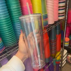 a person is holding a plastic cup in front of colorful plates and cups on display