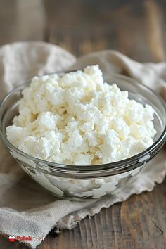 a glass bowl filled with cottage cheese sitting on top of a wooden table next to a napkin