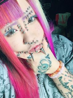 a woman with pink hair and piercings on her face is posing for the camera