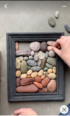 someone is placing rocks in a frame on the ground to make a rock art project