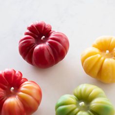 four different colored tomatoes on a white surface