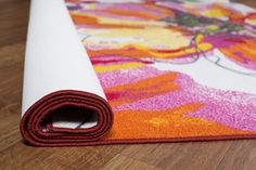 an orange and pink rug on the floor next to a roll of white yoga mat