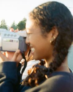 a woman holding a camera up to her face with people in the background looking on