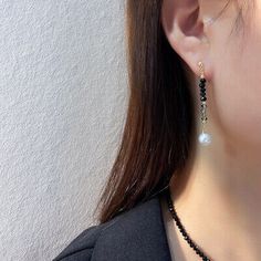 a woman wearing a black and white necklace with pearl drop earrings on her left ear