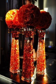 three vases filled with red flowers on top of a black table next to a mirror