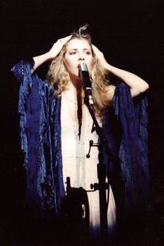 a woman standing in front of a microphone and holding her hands to her head with one hand