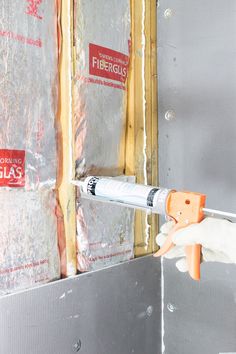 a person in white gloves holding a screwdriver next to a wall with insulation on it