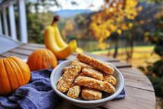 a white bowl filled with granola sitting on top of a wooden table next to pumpkins