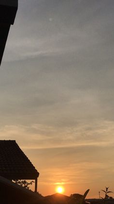 the sun is setting behind a building with a bird perched on it's roof