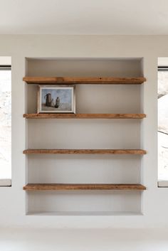 the empty shelves in this room are made out of wood and have two pictures on them