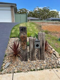 some wooden posts and plants in the middle of a graveled area near a house