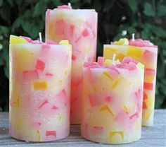 four pink and yellow candles sitting on top of a wooden table next to some bushes