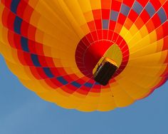 a large colorful hot air balloon flying through the blue sky with no clouds in sight