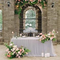 a table with flowers and candles on it in front of a stone wall under an arch