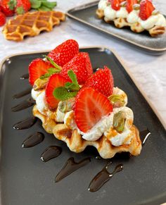 waffles topped with strawberries and whipped cream on a black plate next to chocolate sauce