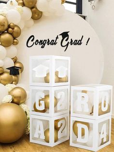 some white and gold balloons are on the wall next to boxes that spell out congrats grad