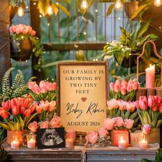 a family is growing by two tiny feet sign surrounded by flowers and candles