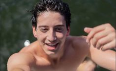 a shirtless young man holding a frisbee in his right hand and smiling at the camera