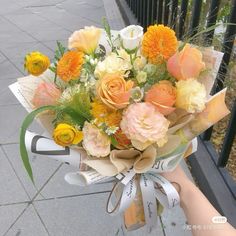 a bouquet of flowers is being held by someone's hand on the sidewalk in front of a fence