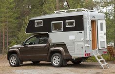 a truck with a camper attached to it parked in front of a wooded area